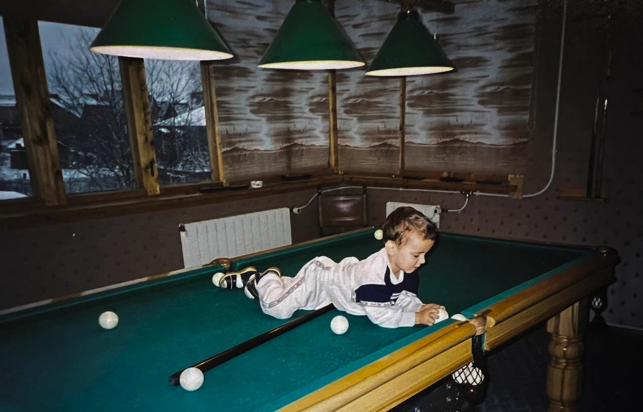 Child playing pool on a green table with pool cues and balls.